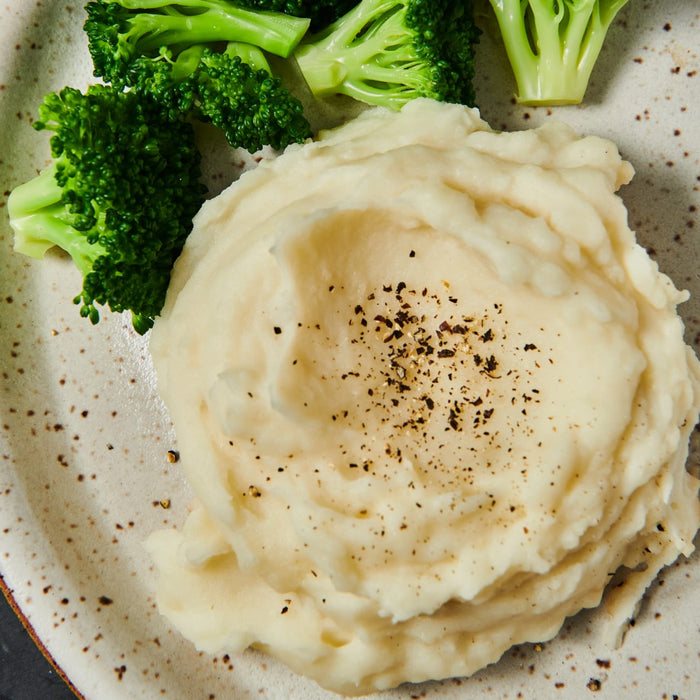 A plate of mashed potatoes with black pepper and broccoli florets.