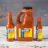 Three bottles of Old Bay hot sauce, one large and two small, are on a white wooden table.