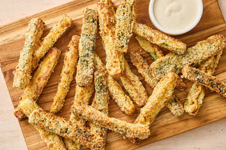 Zucchini fries on a wooden board with a side of dipping sauce