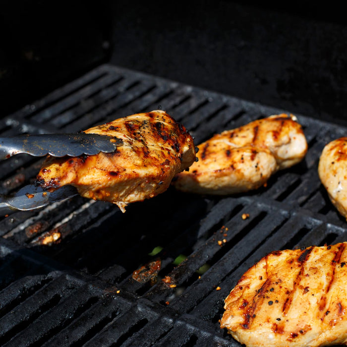 Chicken breasts seasoned with Mccormick Grill Mates Chipotle &amp; Roasted Garlic Seasoning are being grilled, with one piece held by tongs over the hot grates.