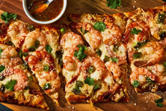 Shrimp flatbread pizza with melted cheese, jalapeños, cilantro, sesame seeds, and dipping sauce