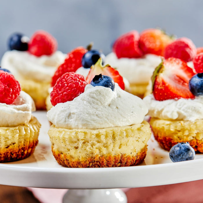 A platter of mini cheesecakes topped with whipped cream and fresh berries.