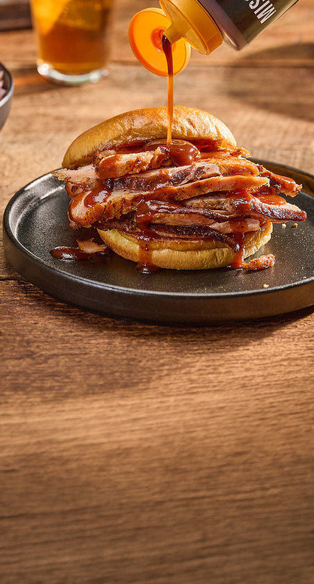 drizzling sauce on a brisket sandwhich