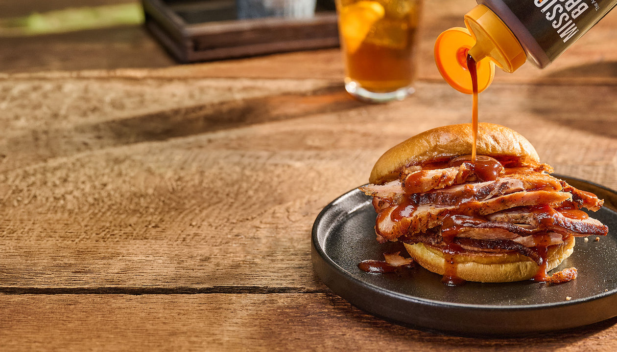 drizzling sauce on a brisket sandwhich