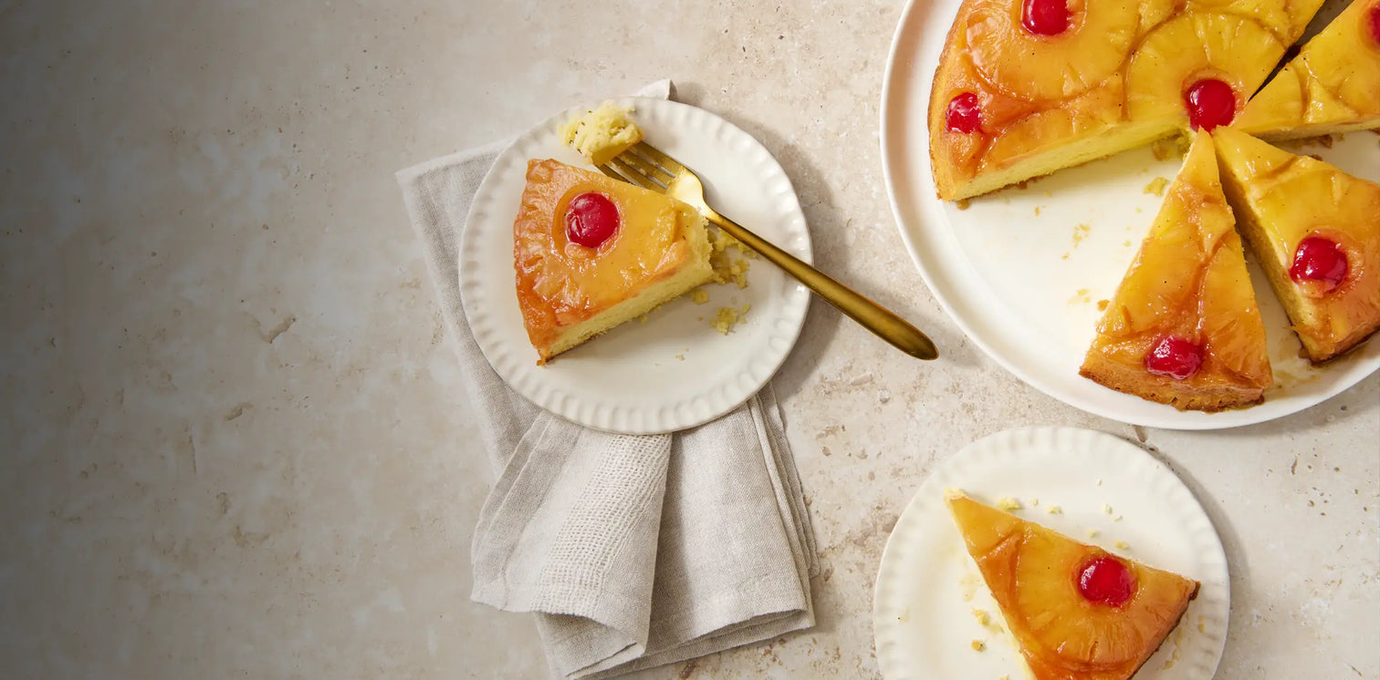 Pineapple upside-down cake with cherry toppings on a light stone surface.