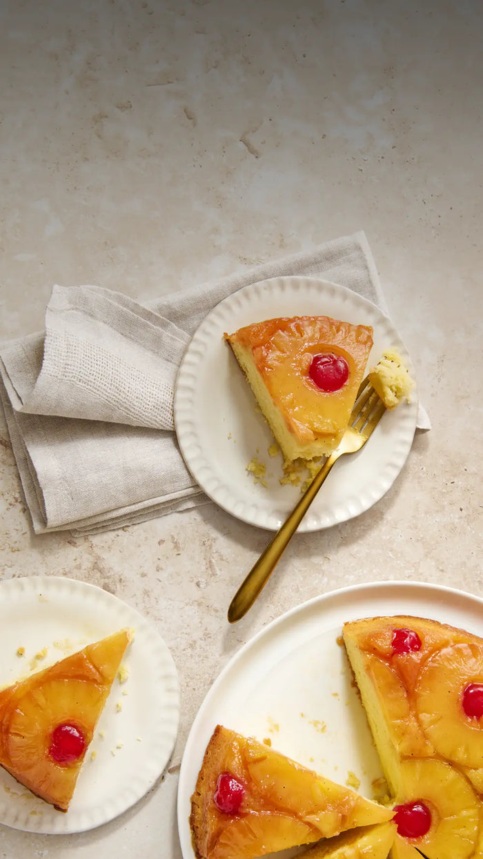 Pineapple upside-down cake with a slice on a plate on a light stone surface.