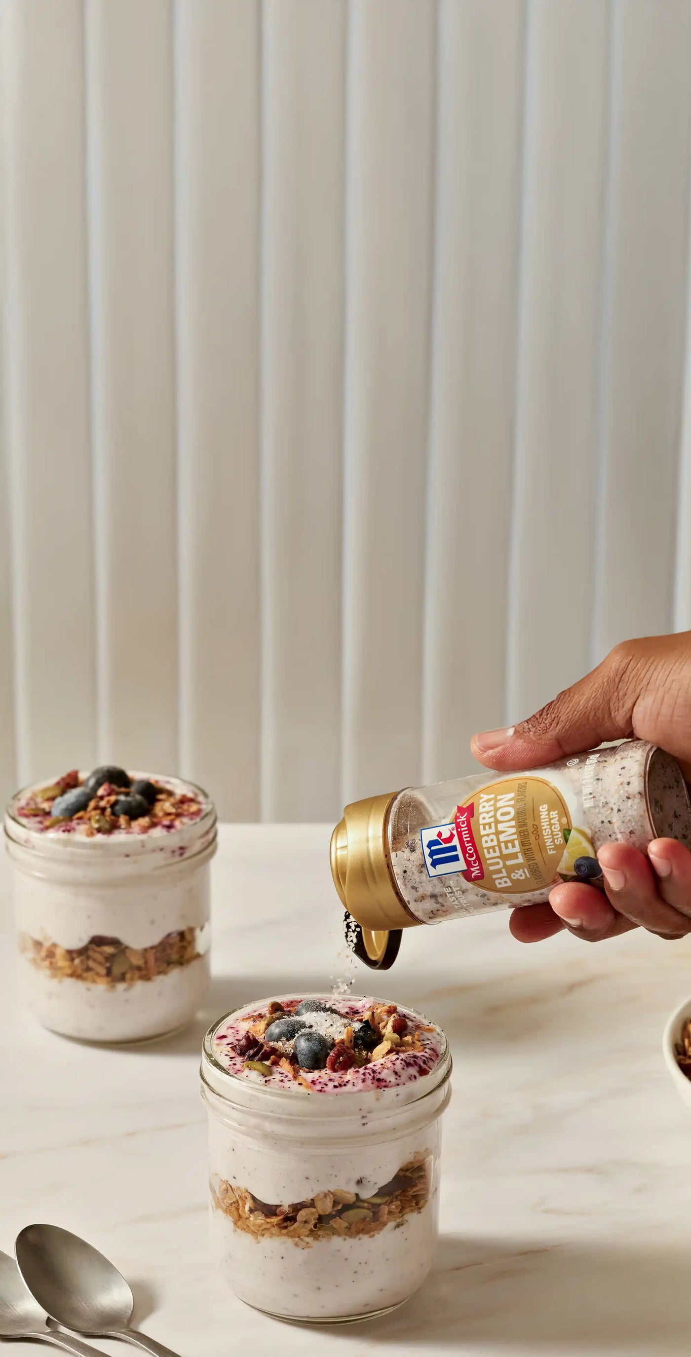 Person pouring finishing sugar into a jar of yogurt parfait on a marble surface