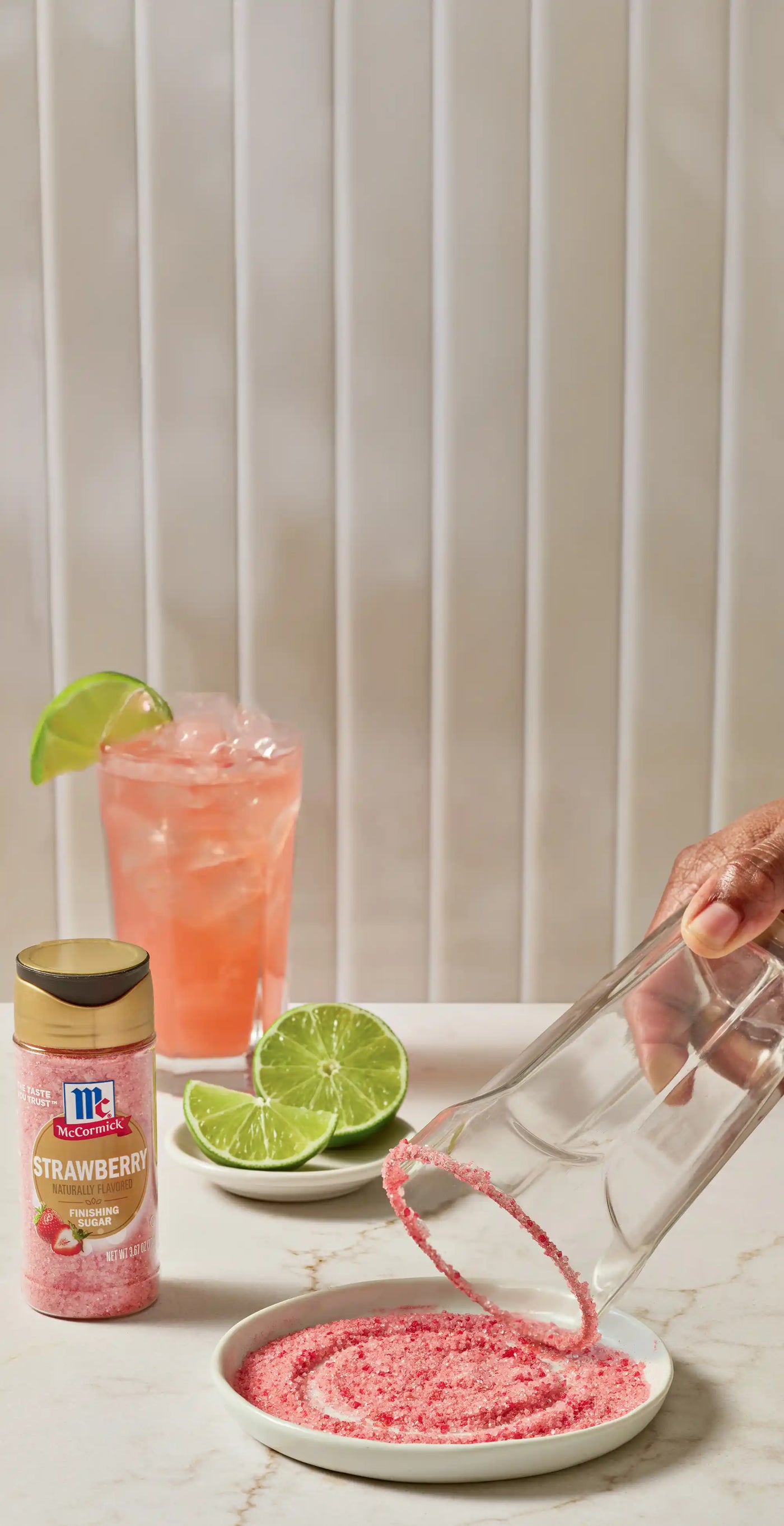 Strawberry finishing sugar bottle with a hand holding a glass that is being rimmed in the pink sugar