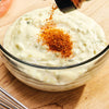 A hand sprinkles McCormick Grill Mates Nashville Hot Chicken Seasoning on a bowl of creamy dip.