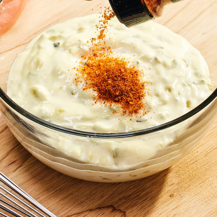 A hand sprinkles McCormick Grill Mates Nashville Hot Chicken Seasoning on a bowl of creamy dip.