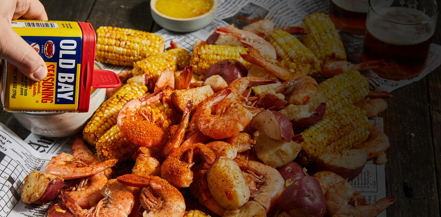old bay sprinkled on a seafood boil with glasses of beer, melted butter all on top of newspaper