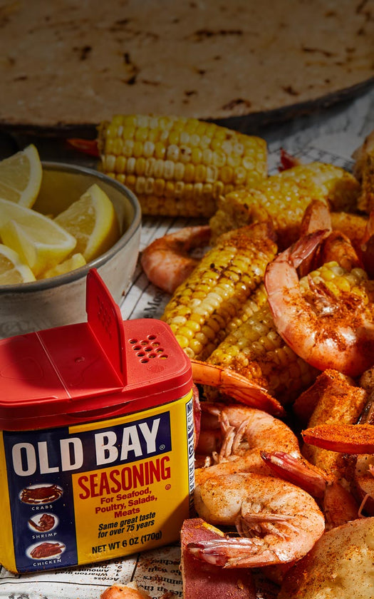 old bay sprinkled on a seafood boil with glasses of beer, melted butter all on top of newspaper