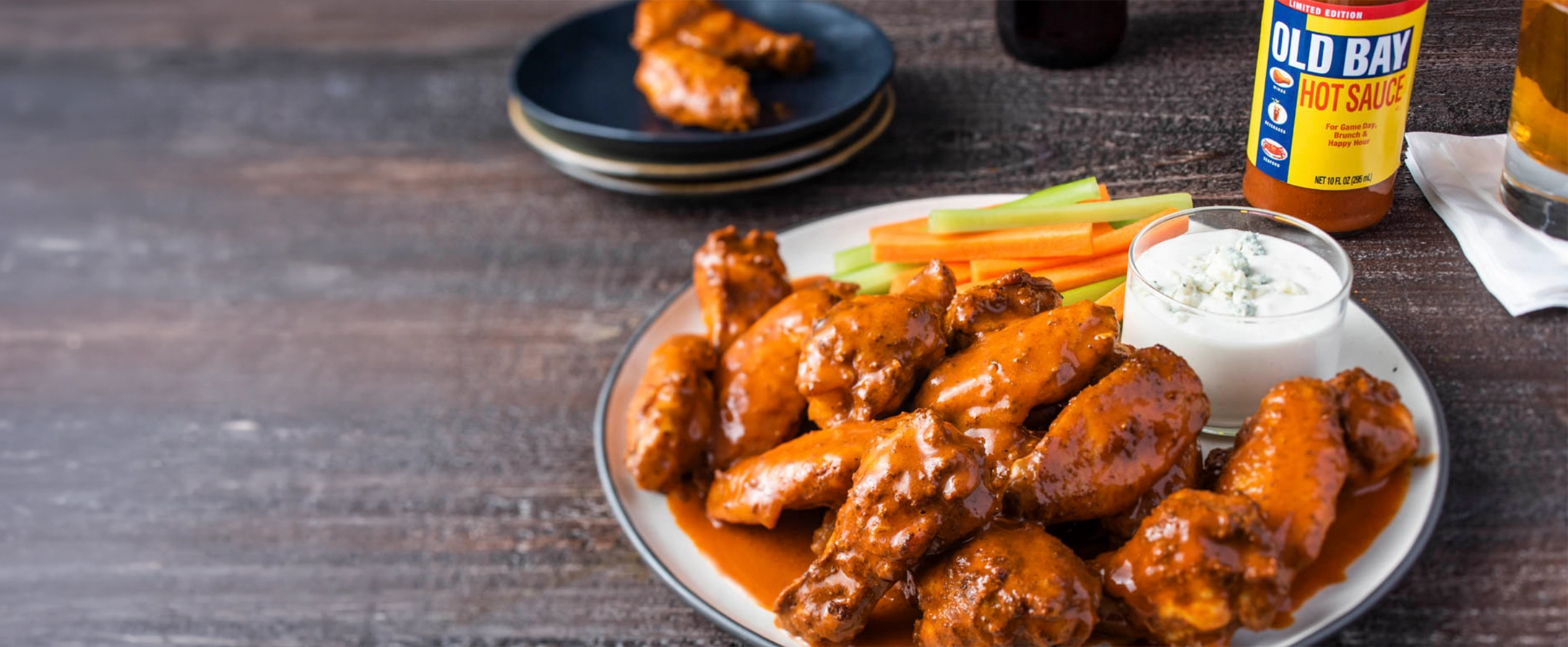 Platter of buffalo wings with celery, carrot sticks, and Old Bay seasoning on a wooden table.