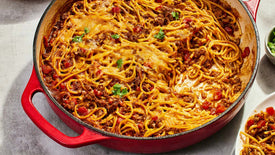 Spaghetti dish in a red pan on a gray surface