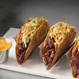 Crispy beef tacos topped with cabbage slaw and creamy orange sauce, served on a white platter with a side of dipping sauce.