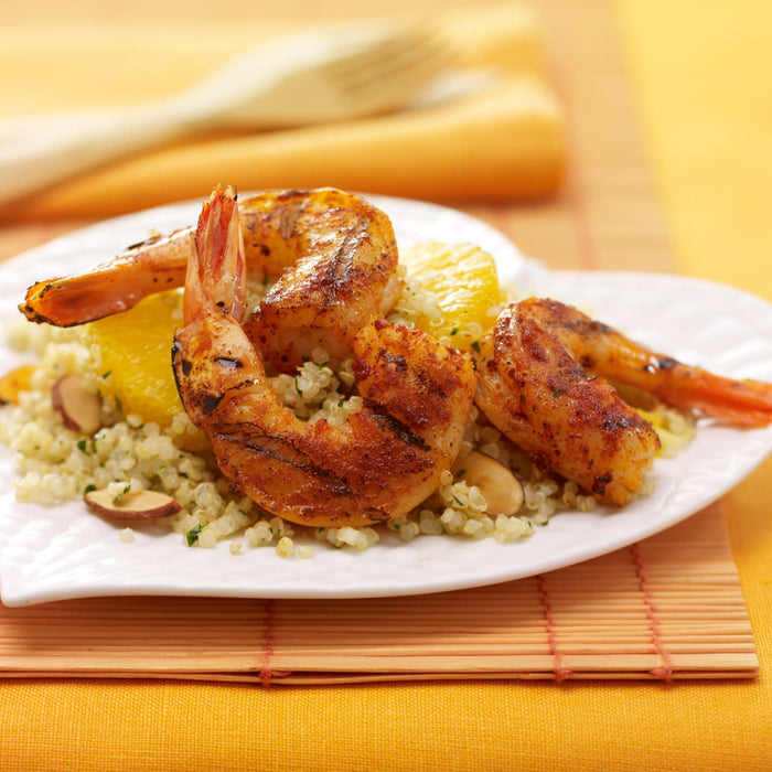 Grilled shrimp seasoned with Lawry'S Casero Paprika Ground are served on a bed of quinoa with orange segments and almonds on a white plate.