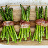 Asparagus spears wrapped in bacon on a wooden cutting board.