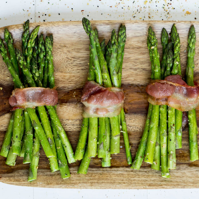 Asparagus spears wrapped in bacon on a wooden cutting board.