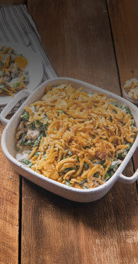 Green bean casserole with fried onions in a white dish on a wooden table.