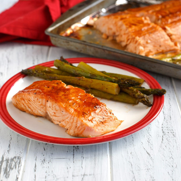 A plate of salmon with asparagus on a white wooden table.