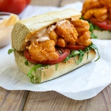 Shrimp po' boy sandwich on a wooden table with a blurred background