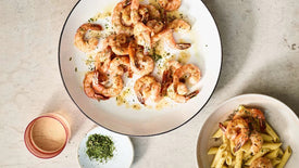 Two bowls of pasta with shrimp on a light stone surface