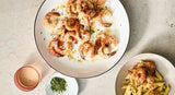Two bowls of pasta with shrimp on a light stone surface