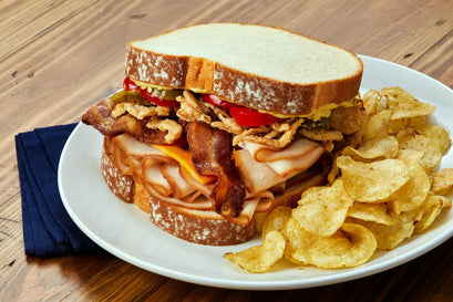 Sandwich with bacon and cheese on a plate with potato chips, on a wooden table.