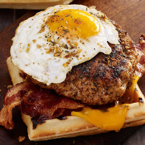 A waffle topped with a sausage patty, bacon, a fried egg, and melted cheese.