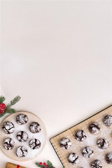 Chocolate crinkle cookies on a baking sheet and plate with a light background