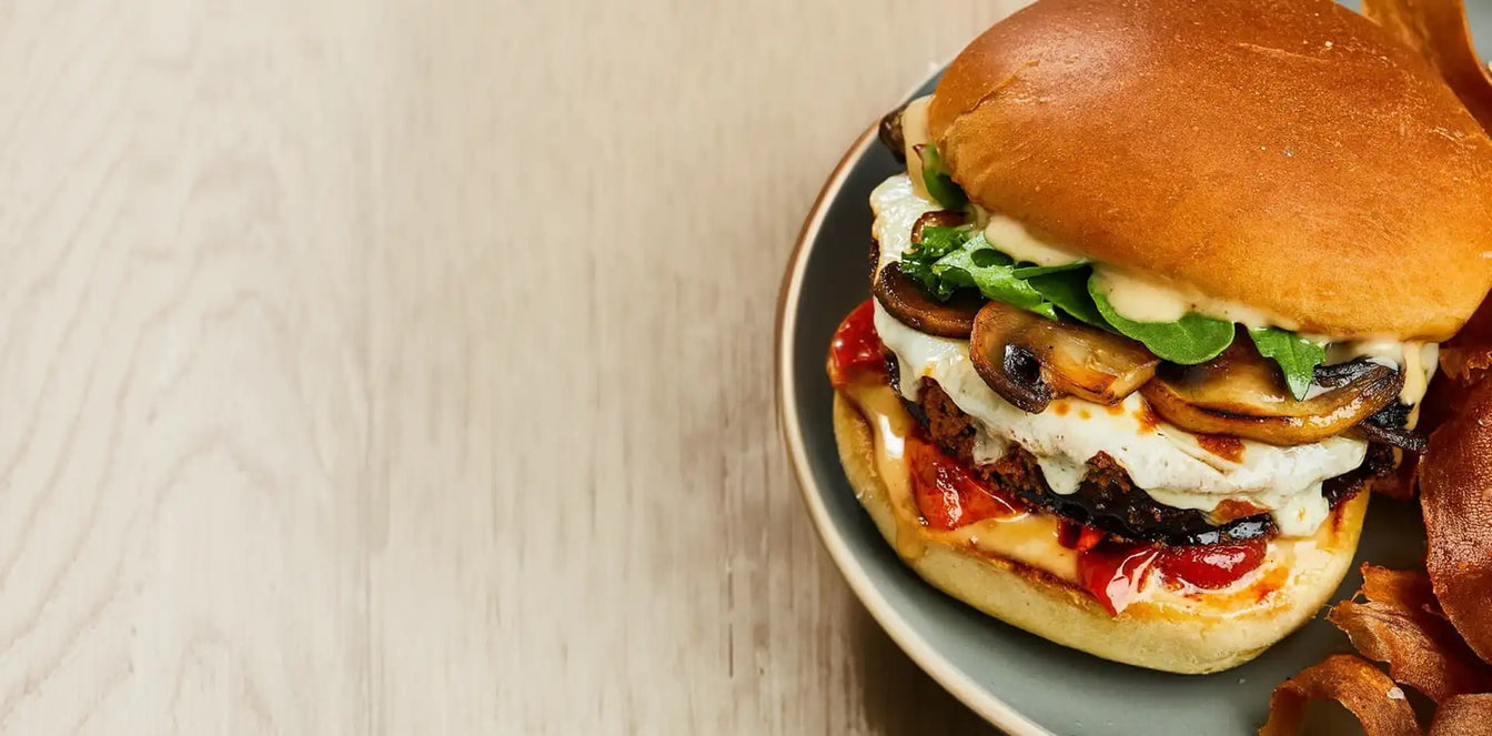Delicious burger with various toppings on a plate against a neutral background