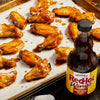 A bottle of Franks RedHot Wings sauce next to a baking sheet of chicken wings.