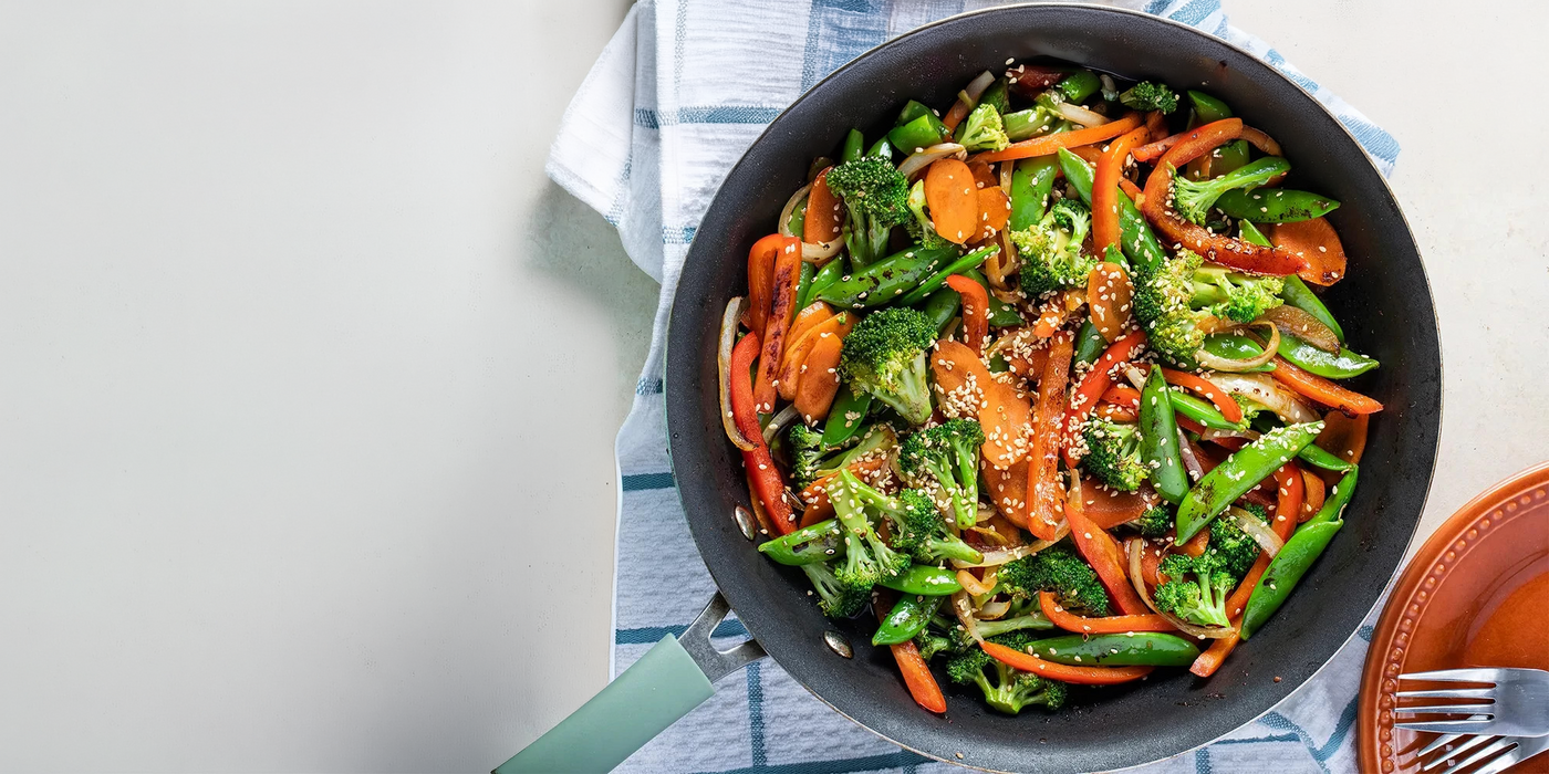 Fried vegetable stir-fry in a black pan on a white background