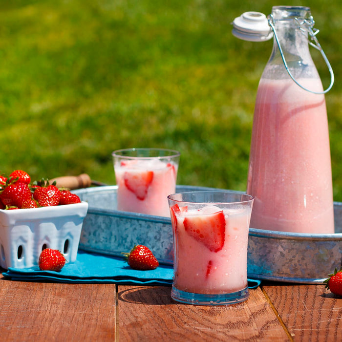 Two glasses of strawberry milk and a pitcher of strawberry milk on a wooden table with strawberries.