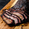 A close up of a sliced brisket on a wooden cutting board.