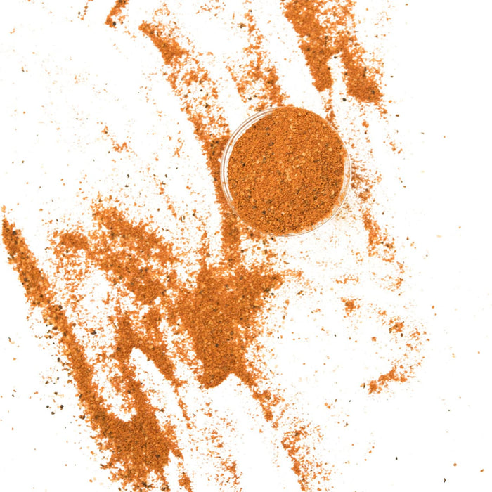 A small bowl of spices sits on a white surface with a trail of spices leading away from it.
