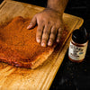 A hand rubs a piece of meat with Stubbs BBQ Rub seasoning.