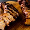 Two pieces of grilled chicken are sliced and arranged on a wooden cutting board.