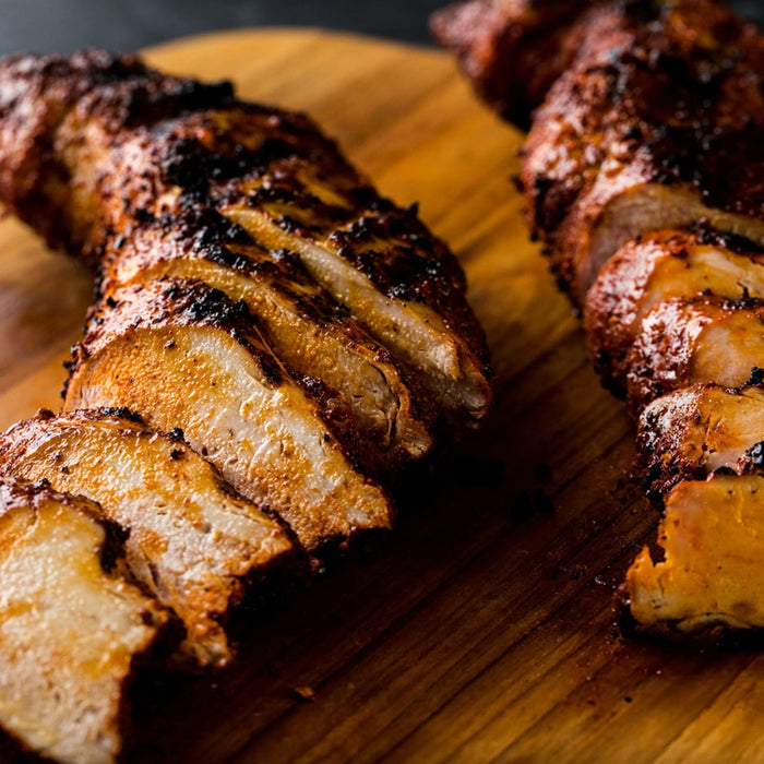 Two pieces of grilled chicken are sliced and arranged on a wooden cutting board.