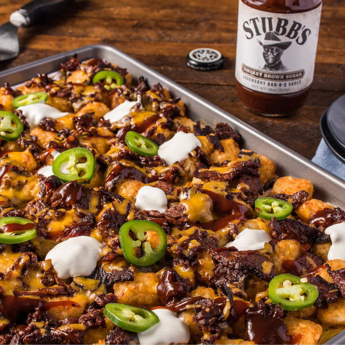A close-up of a plate of tater tots topped with Stubbs BBQ sauce, cheese, jalapenos, and sour cream.