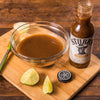 A bottle of Stubbs Chicken Marinade Citrus &amp; Onion with a bowl of marinade and lime wedges on a wooden cutting board.