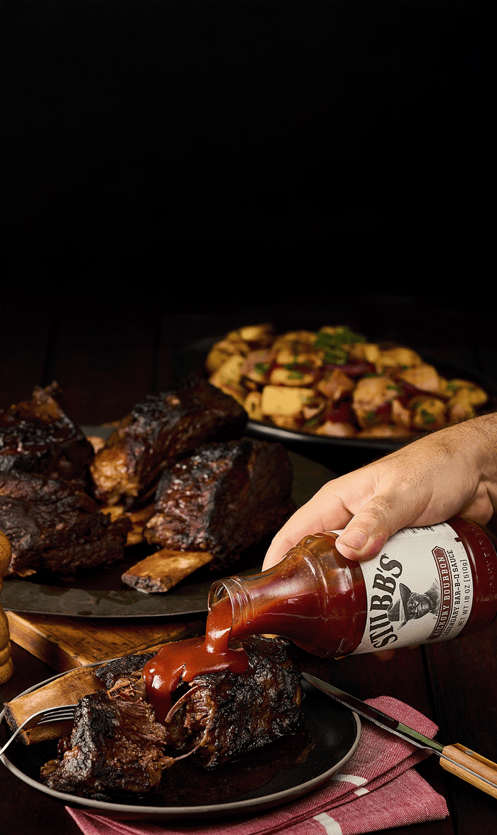 Person pouring sauce onto ribs with a dark background