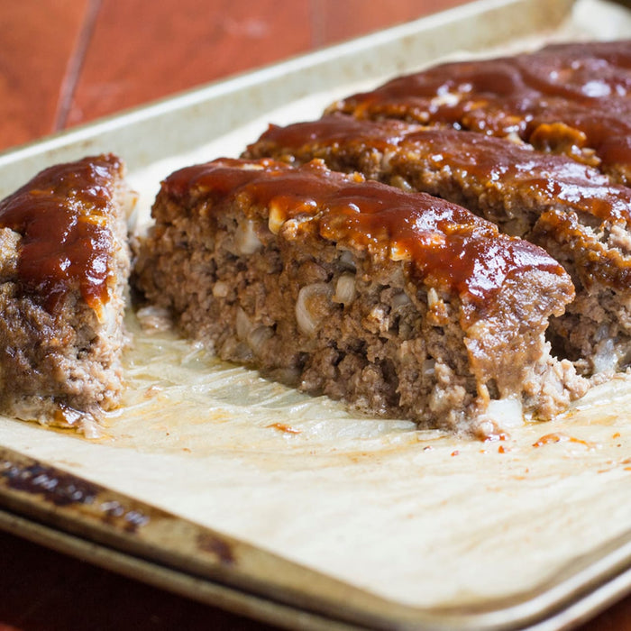 A close up of a meatloaf sliced on a baking sheet.