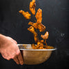 A hand holds a bowl of chicken wings as more wings fall into the bowl.