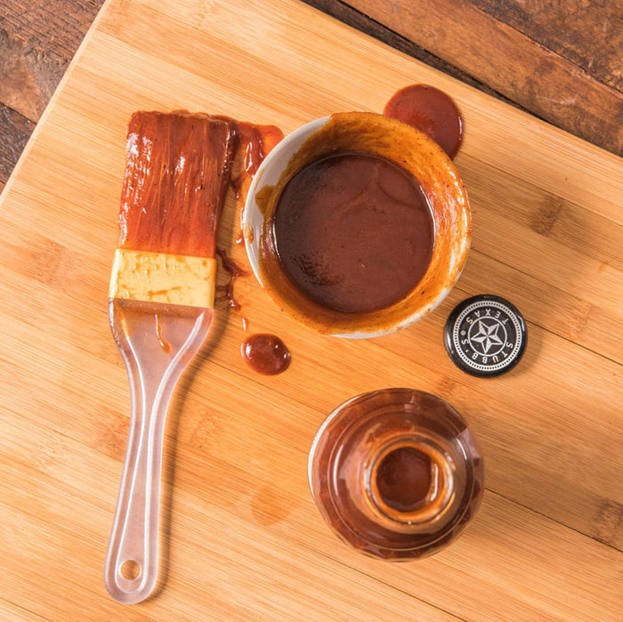 A close-up of a Texas Style BBQ sauce with a brush and a bottle of sauce.