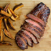 A close-up of a sliced steak with sweet potato fries on a wooden cutting board.