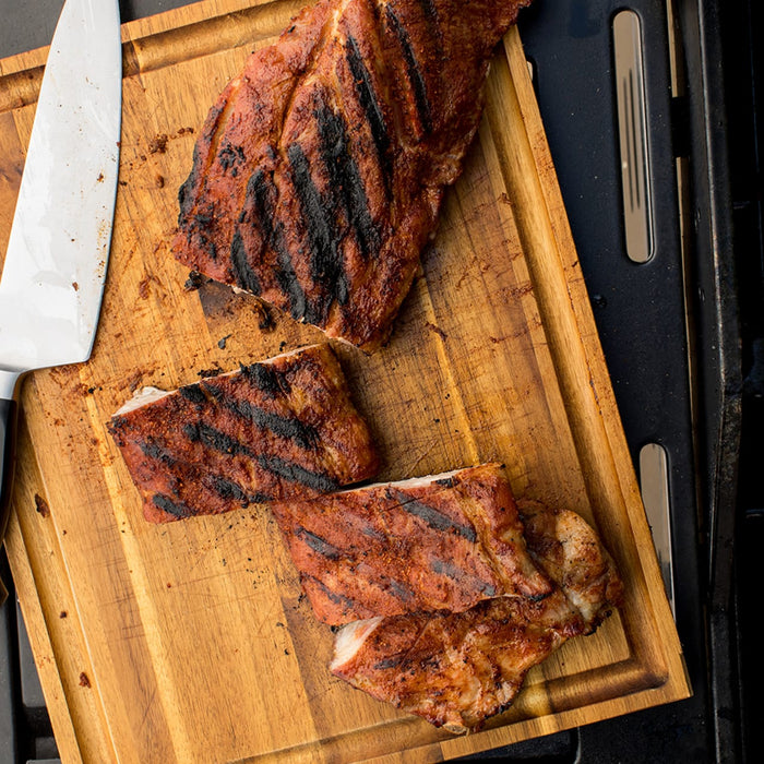 A close-up of a wooden cutting board with four pieces of grilled ribs and a silver knife.