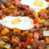 A close-up of a skillet filled with breakfast hash with eggs, sausage, peppers, and onions.