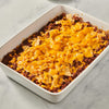 A white casserole dish filled with a cheesy beef and corn mixture topped with tortilla chips.