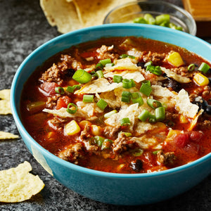 A bowl of chili topped with tortilla chips and green onions.